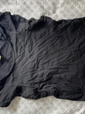 Svart topp med spetsdetaljer - Snygg svart topp med spetsdetaljer vid ärmsluten. Modellen är ärmlös med rund halsringning och har en enkel, stilren design. Perfekt att matcha med jeans eller kjol för en trendig look.