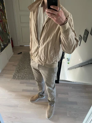Oscar Jacobson vindjacka - Hej! Säljer denna stilrena beigea vindjackan från Oscar Jacobson med dragkedja framtill, två innerfickor med dragkedja, två sidofickor och ribbade muddar vid ärmslut och midja. Jag är 182cm och väger 68kg.😊Storleken är 50 vilket motsvarar ungefär M-L. Mycket gott skick och är i helhet fin och som ny förutom vid muddarna som det är pytte  lite slitet.  Passar utmärkt till ett par beigea chinos nu till våren/sommaren! 🙌 varmt välkommen att höra av dig! Mvh DS 