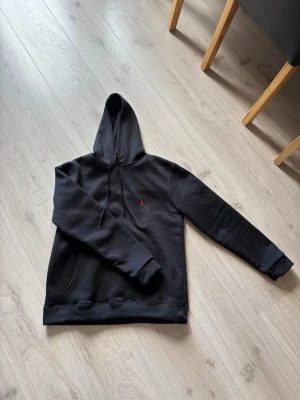 Svart hoodie från Polo Ralph Lauren - Snygg svart Polo Ralph Lauren hoodie med klassisk huva och dragsnören. Liten röd logga broderad på bröstet och känguruficka framtill. 