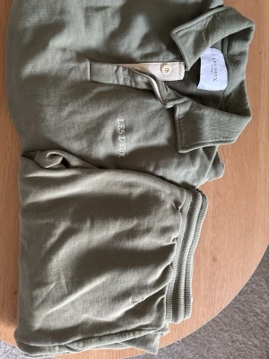 Olivgrönt loungewear-set Les Deux - Snyggt olivgrönt loungewear-set från Les Deux med pikétröja och matchande byxor. Tröjan har krage, knappslå och broderad logga på bröstet. Byxorna har resår i midjan och mjukt material för maximal komfort. 