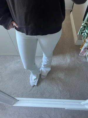 Vita bootcut jeans - Säljer ett par vita bootcut jeans med hög midja och utsvängda ben. Jeansen har en klassisk femficksdesign och är tillverkade i ett stretchigt denimtyg som sitter snyggt. Perfekta för dig som vill ha en clean och fräsch look. Jeansen har slits på insidan