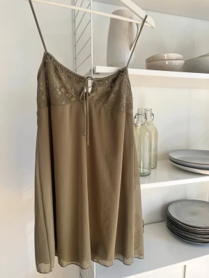 Olivgrön klänning med spetsdetaljer - Söt olivgrön kort klänning, tunna axelband och spets upptill. Säljer då den tyvärr aldrig använts💕
