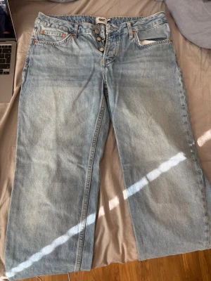Ljusblå raka jeans från 157 - Säljer ett par ljusblå jeans från 157 med raka ben. Jeansen har klassisk femficksdesign, knäppning med knappar och detaljer i kopparfärg. Tillverkade i kraftigt denimtyg som ger en avslappnad och trendig look. Lite sönder trampade längst ner.