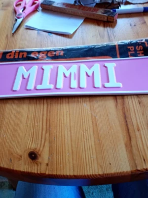 Rosa namnskylt MIMMI/bilskylt - Säljer en personlig namnskylt i plåt  med texten MIMMI i vita bokstäver på rosa bakgrund. Skylten är rektangulär och passar perfekt för dörr eller rum. /Bil.Enkel att sätta upp och ger en personlig touch till inredningen.