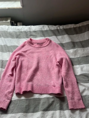 Ljusrosa stickad tröja - Mysig ljusrosa stickad tröja med rund hals och långa ärmar. Tröjan har ribbade muddar vid ärmslut och nederkant, samt en mjuk och fluffig känsla. Perfekt för lager på lager och en söt vardagslook.