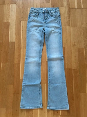 Ljusblå flared jeans - Säljer ett par ljusblå flared jeans med klassisk femficksdesign och normalhög midja. Jeansen har utsvängda ben och är tillverkade i mjukt denimtyg. Perfekta för dig som gillar retrovibbar och en avslappnad stil.
