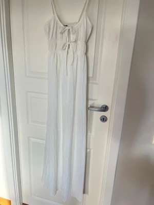 Vit långklänning med rosetter - Lång, vit klänning med smala axelband och två dekorativa rosetter framtill