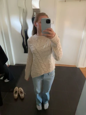 Beige kabelstickad tröja - Säljer en beige kabelstickad tröja med rund hals och långa ärmar. Tröjan har ett snyggt mönster med olika stickade strukturer. Perfekt för att hålla sig varm och stilsäker under kyliga dagar.