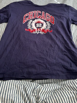 Mörkblå Chicago t-shirt - Snygg mörkblå t-shirt med stort tryck på bröstet där det står 'CHICAGO' och '92 EST' i rött och vitt. Klassisk passform och rund hals. Perfekt för dig som gillar sportig och avslappnad stil.