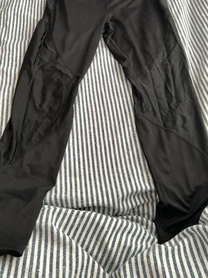 Svarta sportiga leggings - Säljer ett par svarta leggings med sportig look. De har en åtsittande passform och är tillverkade i ett stretchigt material som passar perfekt till träning eller chill. Snygga paneldetaljer längs benen för extra stilpoäng.