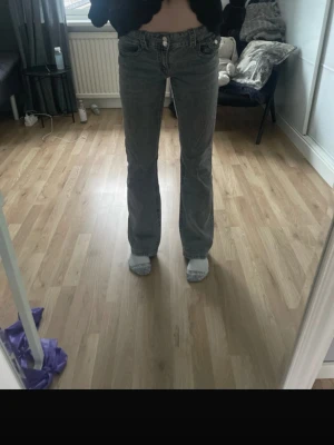 Grå bootcut jeans med låg midja - Säljer ett par gråa bootcut jeans med låg midja och klassisk femficksdesign. Jeansen har en lätt utsvängd passform nedtill och stängs med knapp och dragkedja. Perfekta för dig som gillar en avslappnad men trendig look.