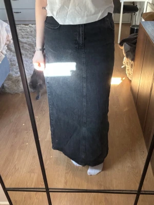 Svart lång jeanskjol med hög midja - Säljer en svart lång jeanskjol med hög midja och klassiska fickor fram. Kjolen har en rak passform och en slit baktill. Kjolen är från OBJECT, beställd på Nelly! Använd men inga defekter🖤