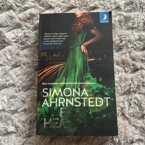 En enda hemlighet av Simona Ahrnstedt - Säljer boken 'En enda hemlighet' av Simona Ahrnstedt. Omslaget har en kvinna i grön klänning mot en mörk bakgrund med stadsljus. Pocketbok på svenska från Månpocket, perfekt för dig som gillar romantik och spänning.