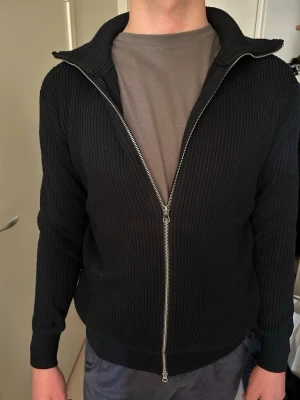 Marinblå ribbad ziptröja - Säljer en marinblå ribbad ziptröja med hög krage och dubbel dragkedja. Grov stickat material. Den är i bra skick! 