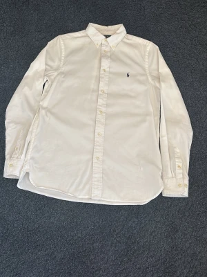 Vit skjorta från Ralph Lauren - Klassisk vit skjorta från Ralph Lauren med button-down krage och broderad logga på bröstet. Skjortan har lång ärm, knappar framtill och är tillverkad i mjuk bomull. Perfekt till en clean och stilren look.