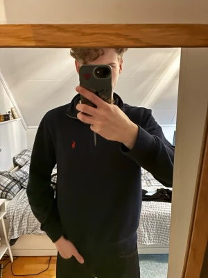 Mörkblå quarter-zip tröja Polo Ralph Lauren - Snygg mörkblå half-zip tröja från Polo Ralph Lauren med röd broderad logga på bröstet. Tröjan har hög krage och dragkedja framtill. 