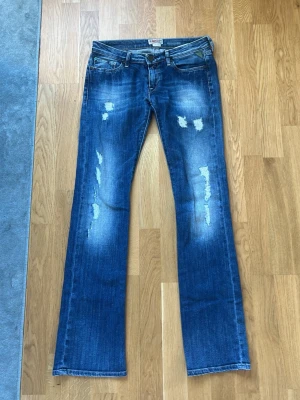 Blå low waist straight leg jeans från replay - Säljer ett par snygga blå bootcut jeans från Replay med slitna detaljer och tvättade partier framtill. Hålet där bak är igen sytt. Köpt från Sellpy och passade inte mig. 