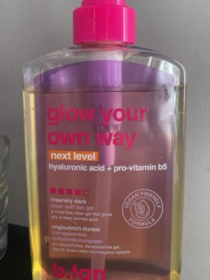 b.tan brun utan sol - Transparent brun utan sol-gel från b.tan med hyaluronsyra och pro-vitamin B5. Ger en djup bronsfärg och är vegansk. Kommer i en genomskinlig plastflaska med rosa pump och text i rosa och vitt.  Helt ny