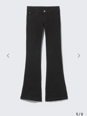 Svarta bootcut jeans från weekday - Säljer ett par svarta bootcut jeans från weekday med klassisk femficksdesign och utsvängda ben. Jeansen har en liten rosa patch bak och är tillverkade i stretchigt material för extra komfort. Perfekta för dig som gillar en retroinspirerad look.