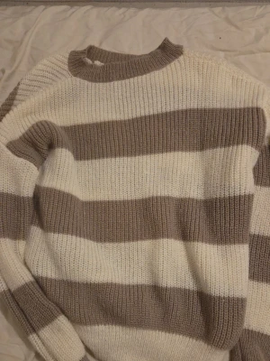 Randig beige och vit stickad tröja - Säljer en oversized stickad tröja med breda beige och vita ränder. Tröjan har rund halsringning och är ribbstickad för extra mysfaktor. Perfekt för lager på lager och chill stil.