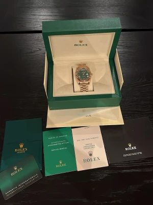  Day-Date guld med grön urtavla - Exklusiv  Day-Date i guld med grön urtavla och romerska siffror. Klockan har President-länk och klassisk räfflad bezel. Levereras i originalbox med certifikat och tillbehör. Perfekt för dig som vill ha något riktigt lyxigt på handleden.
