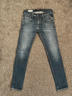 Blå Replay anbass slim fit jeans med slitningar - Säljer ett par blå slim fit jeans med snygga slitningar och tvättade detaljer. Klassisk femficksmodell med normalhög midja och smal passform hela vägen ner. Jeansen har en modern look och passar perfekt till sneakers eller boots. Materialet är mjukt och stretchigt för extra komfort. W30 L32