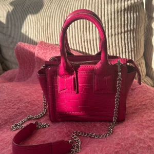 Rosa Handväska  - Snygg liten handväska i rosa med croco-mönstrad yta. Den har använts flitigt så har någon liten repa men inget som syns, men den har varit väl omhändertagen🩷