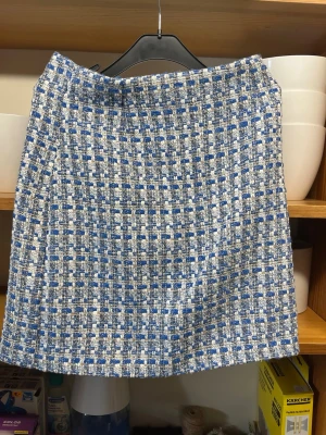 Blåvit rutig kortkjol i tweed - Säljer en snygg blåvit kortkjol i rutigt tweedtyg. Kjolen är aldrig använd men har dock ingen prislapp kvar! Storlek XS 34.