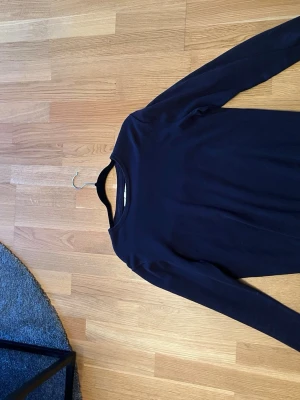 Mörkblå långärmad topp KappAhl - En enkel och stilren mörkblå långärmad topp från KappAhl. Toppen har rund halsringning och är tillverkad i ett mjukt material som känns skönt mot huden. Perfekt att matcha med jeans för en clean look.