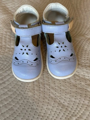 Ljuslila sandaler med blommönster - Söta ljuslila sandaler från KAVAT i mjukt läder med dekorativa blommönster och hål på ovandelen. Kardborreband gör dem enkla att ta på och av. Vita kanter och innersula i skinn ger en fräsch look. Perfekta för varma dagar.