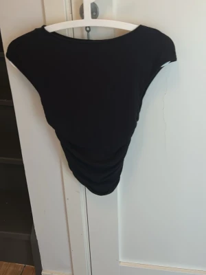 Svart tröja med scrunchade sidor - Säljer en svart tröja med rund halsringning och rynkade sidor. Tröjan har en enkel och stilren design, perfekt att matcha med olika outfits. Tillverkad i mjukt stretchigt material för en bekväm passform.