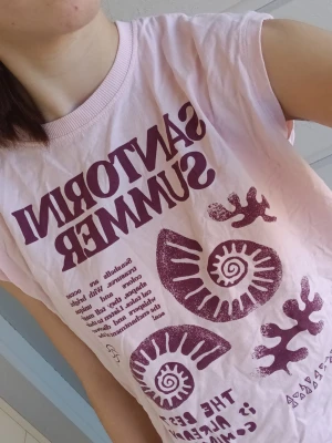 Ljusrosa Santorini Summer t-shirt - Säljer en ljusrosa t-shirt med trycket 'Santorini Summer' från Zara. 👚🌸T-shirten har ett coolt grafiskt mönster med snäckor och koraller, samt text.  🪸🐚Modellen är ärmlös och har en avslappnad passform. Perfekt för dig som gillar unika sommarprints! Storlek 9-10 år.🪷