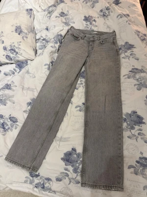 Grå raka jeans med låg midja - Säljer ett par grå lågmidjade jeans med rak passform. Jeansen har klassisk femficksdesign och är tillverkade i denim. Perfekta för en avslappnad och trendig look.