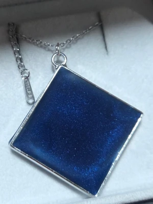 Havsblåskimrande glow kvadratiskt halsband - lyser i mörker!! - Unikt halsband med en stor, kvadratisk blå berlock som har en skimrande yta och silverfärgad ram. Berlocken lyser i mörkret med ett starkt blått sken efter att ha varit i dagsljus en kort stund. Kedjan är tunn och silverfärgad med justerbar längd. Perfekt för dig som gillar coola och iögonfallande accessoarer. 🌸✍️🏻// Handgjord & skapad av mig, tillverkat med högkvalitativt självlysande pigment för ett tydligt sken och lång livslängd. Kedjan och hänget tål vatten och missfärgas inte.