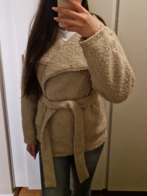 Beige teddyjacka med bälte - Säljer en beige teddyjacka med bred krage och knytbälte i midjan. Helt ny med prislapp! 