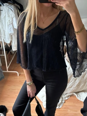 Mörkblå  blus med vida ärmar - Säljer en mörkblå transparent blus med v-ringning och vida, fladdriga ärmar. Blusen har lätt plisserad struktur. 