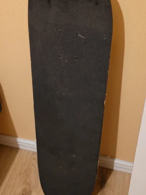 Skateboard med grafiskt mönster - Skateboard med svart grip tape på ovansidan och ett grafiskt mönster i vitt, svart och orange på undersidan. Utrustad med vita hjul och silverfärgade trucks. Perfekt för dig som gillar att cruisa eller göra tricks.