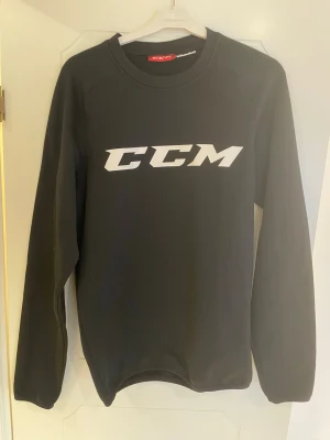 Svart sweatshirt från CCM - Säljer en svart sweatshirt från CCM med stor vit logga på bröstet. Tröjan har rund halsringning och långa ärmar. Perfekt för träning eller chill. Material 94% polyester, 6% elastan.