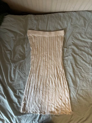 Beige ribbad kjol - Säljer en beige ribbad kjol från SAMSA Collection. Kjolen är lång, har bred resår i midjan och ett snyggt plisserat fall. Perfekt för dig som gillar en enkel men trendig look. Passar till många olika stilar och är superenkel att matcha.