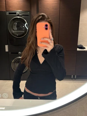 Svart omlottopp med v-ringning - Snygg svart omlottopp med v-ringning och långa ärmar. Toppen är croppad och har en figurnära passform som framhäver midjan. Perfekt att styla med jeans eller kjol för en trendig look.