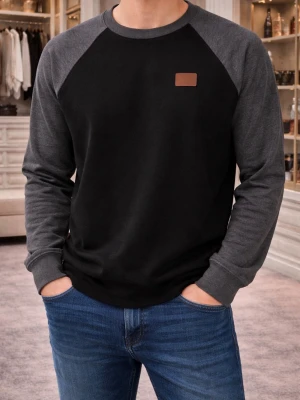 Svart och grå sweatshirt med raglanärm - Säljer en stilren sweatshirt i svart med mörkgrå raglanärmar. Tröjan har rund halsringning och en liten brun patch på bröstet. Tillverkad i mjukt bomullsmaterial som är skönt mot huden. Perfekt för en avslappnad look.