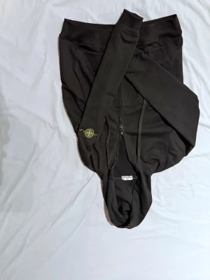 Svart hoodie från Stone Island - Säljer en svart hoodie från Stone Island med den klassiska logotypen på vänster ärm. Hoodien har dragsko i huvan och en enkel, stilren design. Tillverkad i mjukt bomullsmaterial som är skönt att bära. Perfekt för dig som gillar streetwear och vill ha något snyggt och bekvämt.
