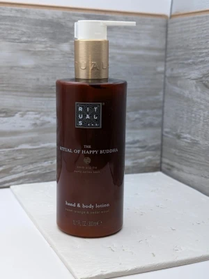 Oöppnad Rituals Happy Buddha hand & body lotion - Oöppnad Hand- och bodylotion från Rituals i serien The Ritual of Happy Buddha. Flaskan är brun med guldfärgad pump och rymmer 300 ml. Doft av söt apelsin och cederträ. Perfekt för dig som vill ha en återfuktande och väldoftande lotion.