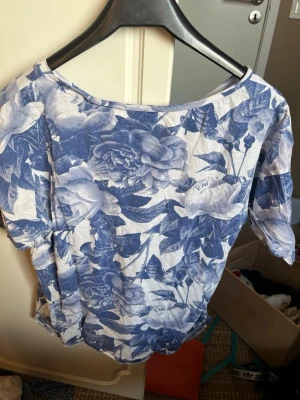Blommig topp från Monki i blått och vitt - Säljer en snygg topp från Monki i storlek S med blått och vitt blommönster. Toppen har rund halsringning och korta ärmar. Perfekt för dig som gillar en avslappnad men trendig stil.