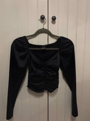 Fest topp  - Trendig svart topp med långa puffärmar och rynkade detaljer framtill. Perfekt till fest. Materialet känns mjukt och stretchigt. XXS men passar även XS eller liten S