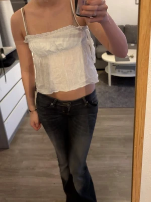 Vit linnetopp med snörning i sidan - Supersöt vit linnetopp med tunna axelband och snörning i sidorna. Toppen är croppad och har en luftig, lätt struktur i bomull. Perfekt för varma dagar och ger en fräsch och trendig look.