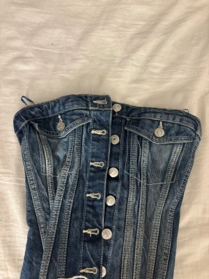 Jeans korsettopp med knappar från Zara - Denim korsettopp i blått med silverfärgade knappar framtill från Zara. Säljer för den inte passade mig har haft den 1 gång annars aldrig använt eftersom det var fel storlek. Nypris 400kr ungefär, priset kan diskuteras.