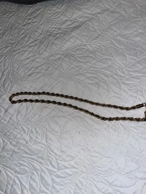 Guldfärgat tvinnat halsband - Säljer ett stilrent guldfärgat halsband med tvinnad kedja. Halsbandet har en klassisk design och är tillverkat i metall med en snygg glansig finish. Perfekt för dig som gillar minimalistiska accessoarer med lite extra detalj.