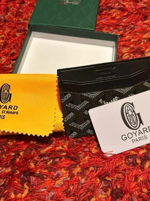 GYärd black wallet - Snyggt svart kortfodral med klassiskt mönster i vitt och grått. Tillverkad i läder och canvas, perfekt för kort och ID. Kommer med original ask och gul putsduk med logga. Stilren och lyxig accessoar.