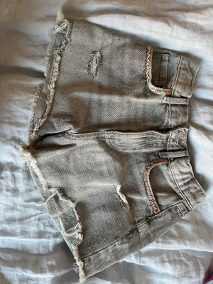 Grå denim shorts med fransar - Säljer ett par grå denim shorts med broderi på fickorna. Perfekta för sommaren